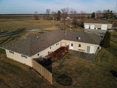 Beige ranch-style house with brown roof and attached garage on a grassy lot, viewed from above.