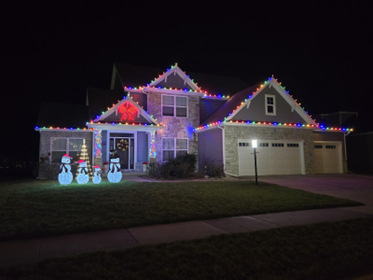 House with colorful Christmas lights on the roof and lawn decorations of snowmen and a Christmas tree, lit up at night.