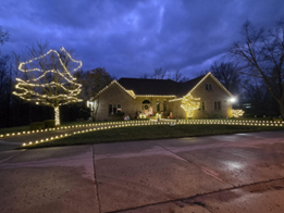House decorated with Christmas lights at dusk, with a tree in the yard also lit.