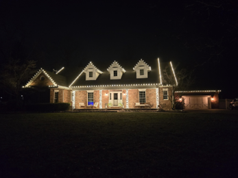 House at night, adorned with white Christmas lights along the roof and windows.