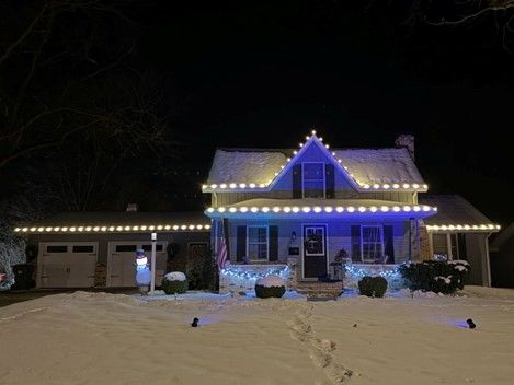 House decorated with blue and yellow Christmas lights, in a snowy setting at night.