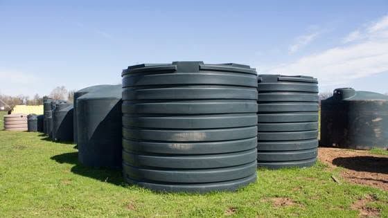 Large black plastic water tanks stacked on grass in an outdoor field under a clear sky