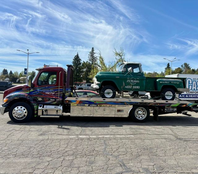 Tow truck hauling a vintage green pickup on a flatbed under a blue sky