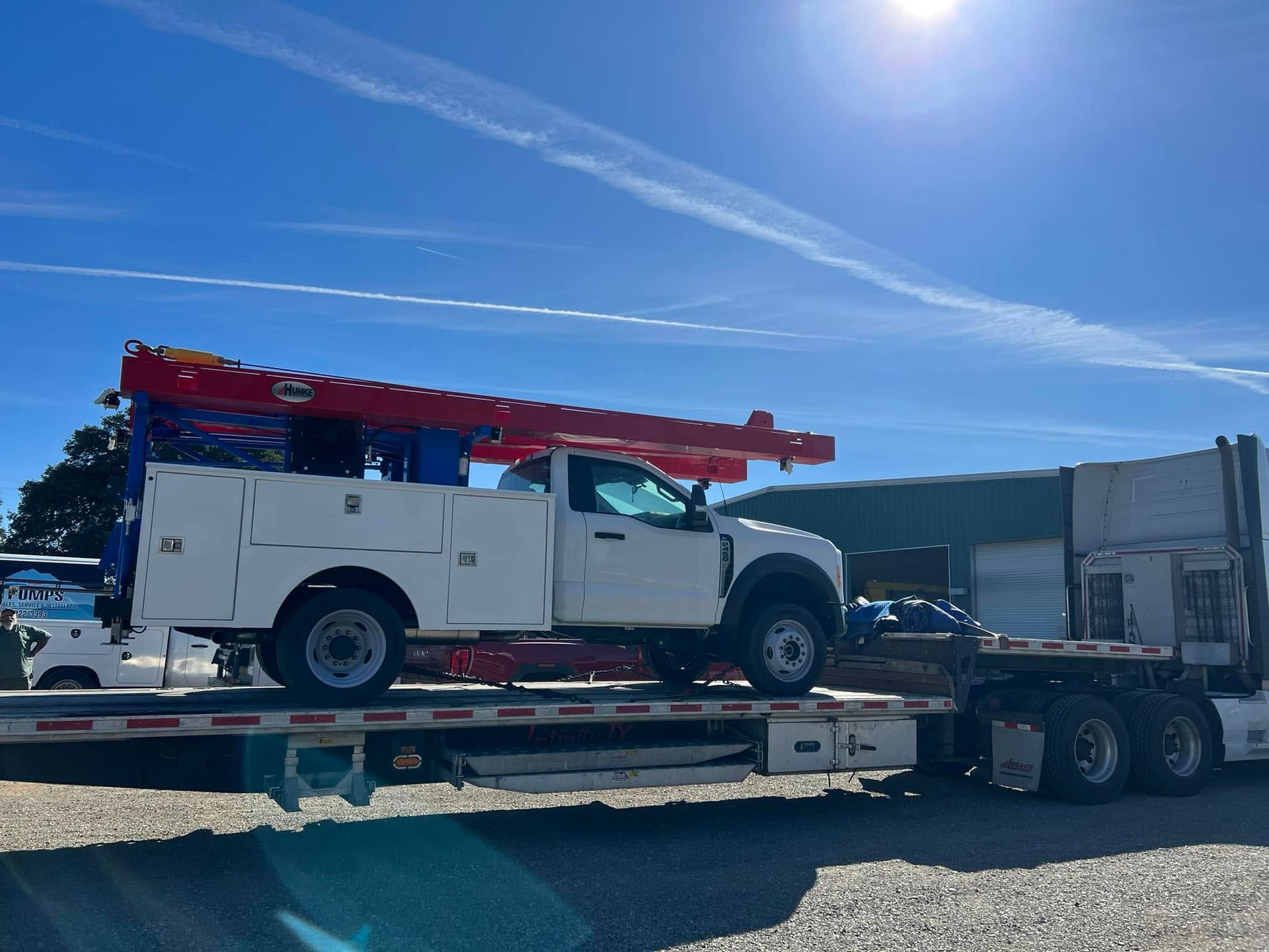 White utility truck with red ladder rack on a flatbed trailer under a bright blue sky