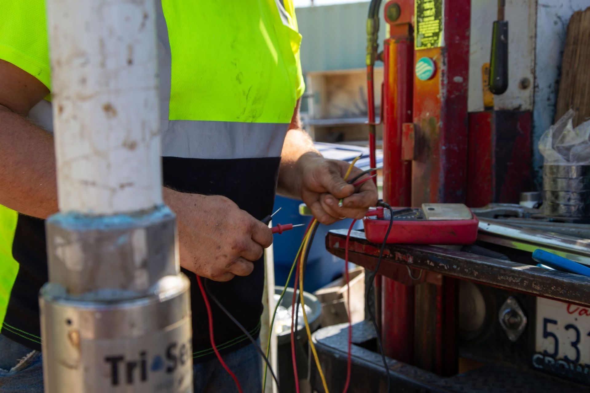 Worker in a neon vest wiring equipment beside a red machine on a truck bed