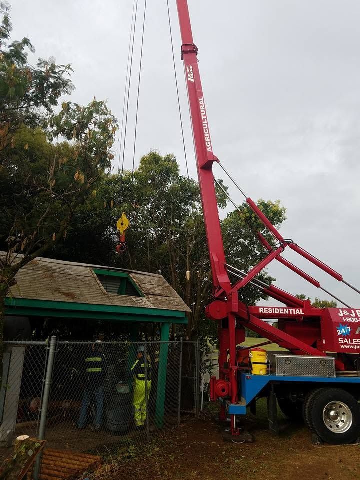 Red crane lifting debris beside a small green-roofed building in a cloudy outdoor area