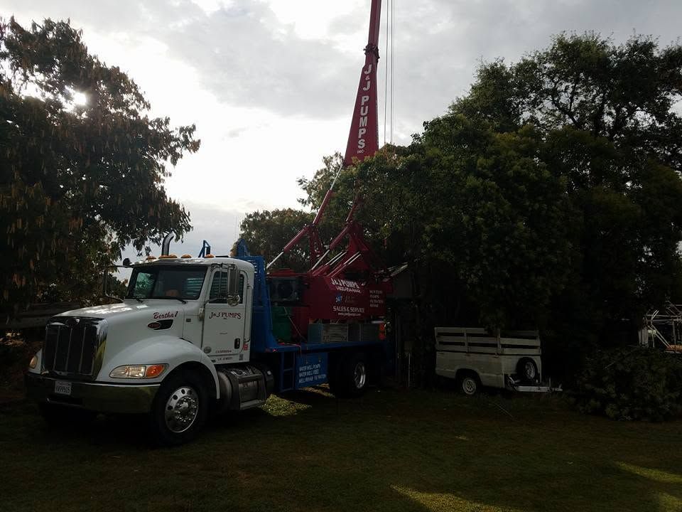 Large white truck with red drilling rig parked on grass beside trees and a small white van