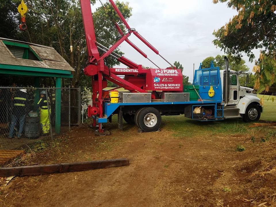 Red utility truck with crane parked by a wet roadside beside a building and trees