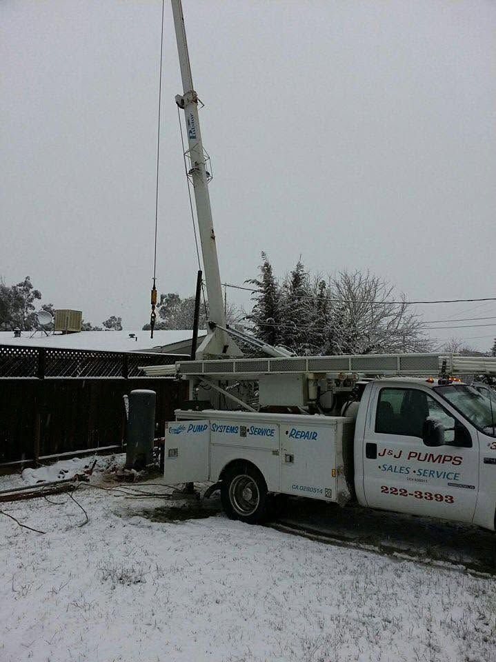 Bucket truck parked in snowy yard beside a building, with its boom raised into the gray sky