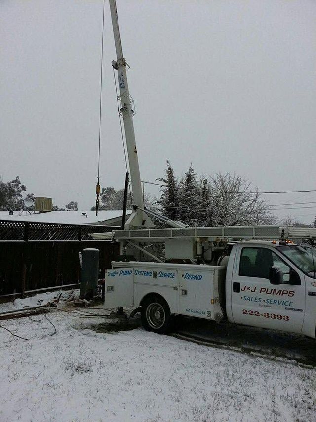 Utility truck with raised crane in a snowy yard beside a fence and trees.