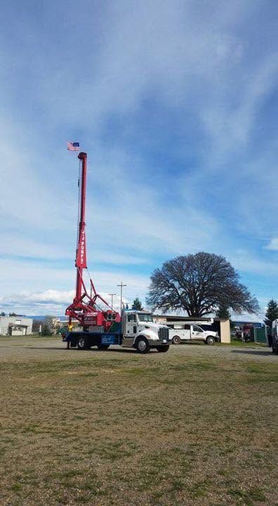 White truck with red drilling rig in a grassy field under a blue sky.