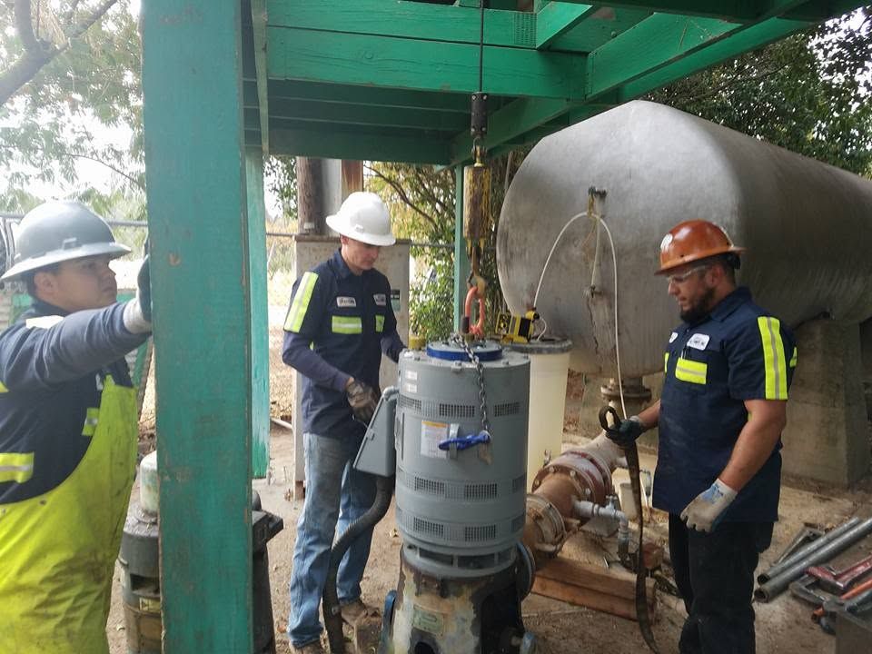 Workers in hard hats inspecting industrial equipment under a green metal canopy.