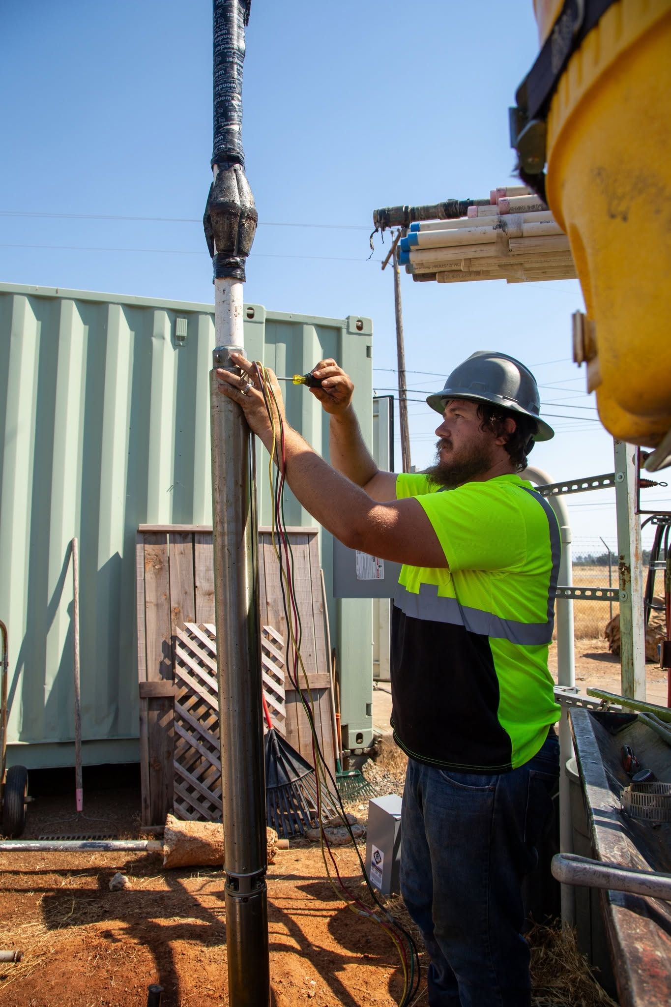 Worker in neon shirt and hard hat adjusting a vertical pipe at a construction site