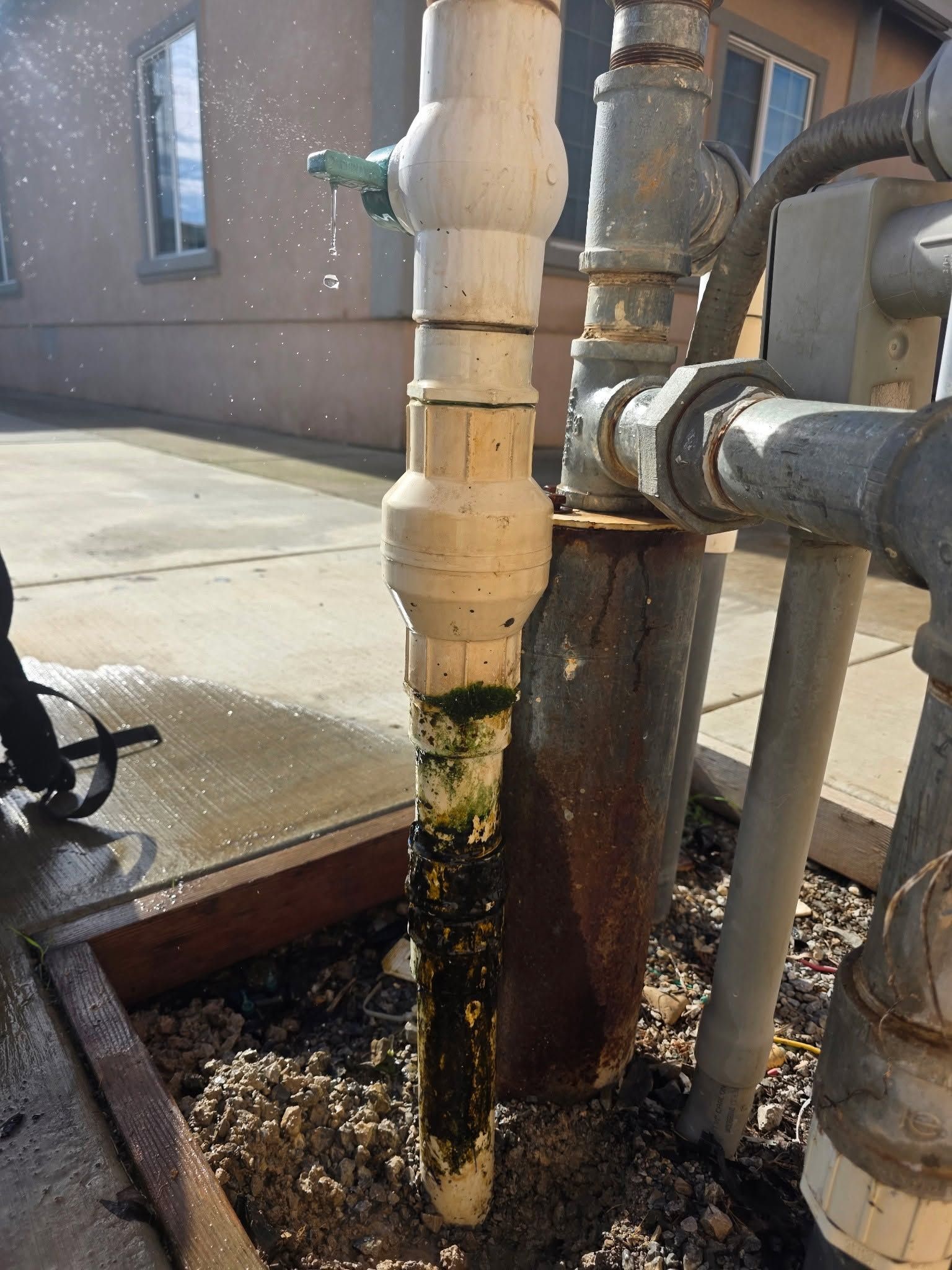 Outdoor utility pipes with rust and leaking water beside a building.