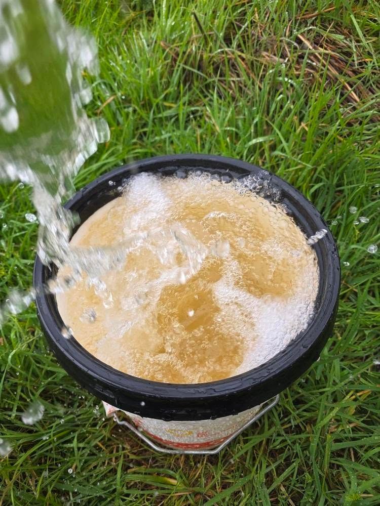 Water pouring into a black bucket of muddy water sitting on grass