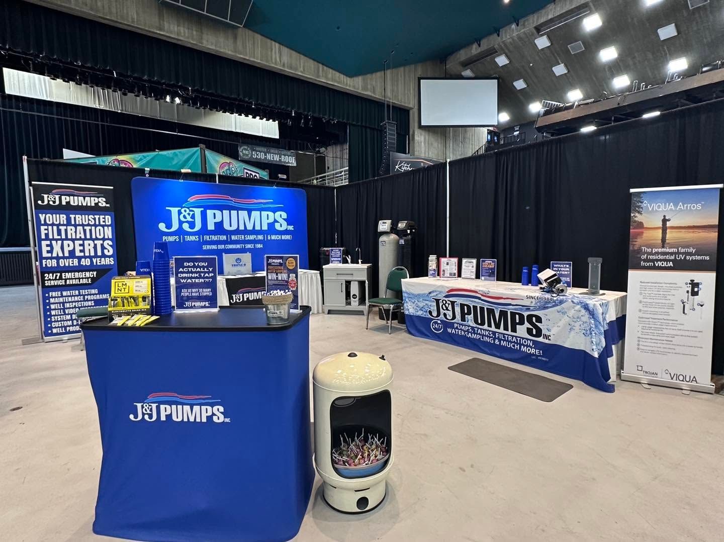 J&P Pumps trade show booth with blue banners, counter, display stands, and a rain barrel in a convention hall