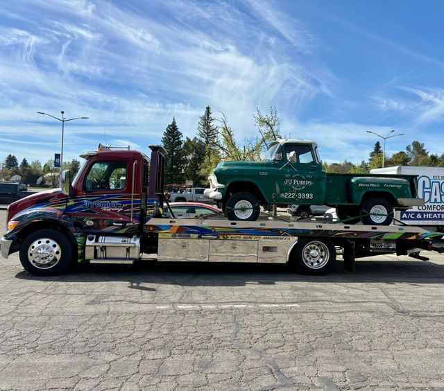 Tow truck hauling a vintage green pickup on a flatbed under a blue sky