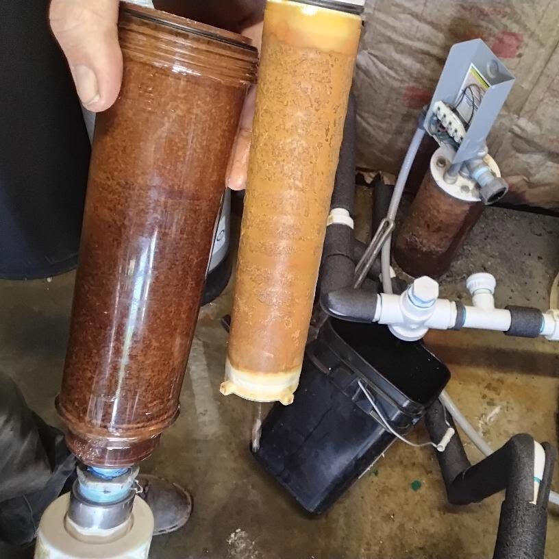 Two large translucent filter canisters connected to white pipes beside a sink and black basin.