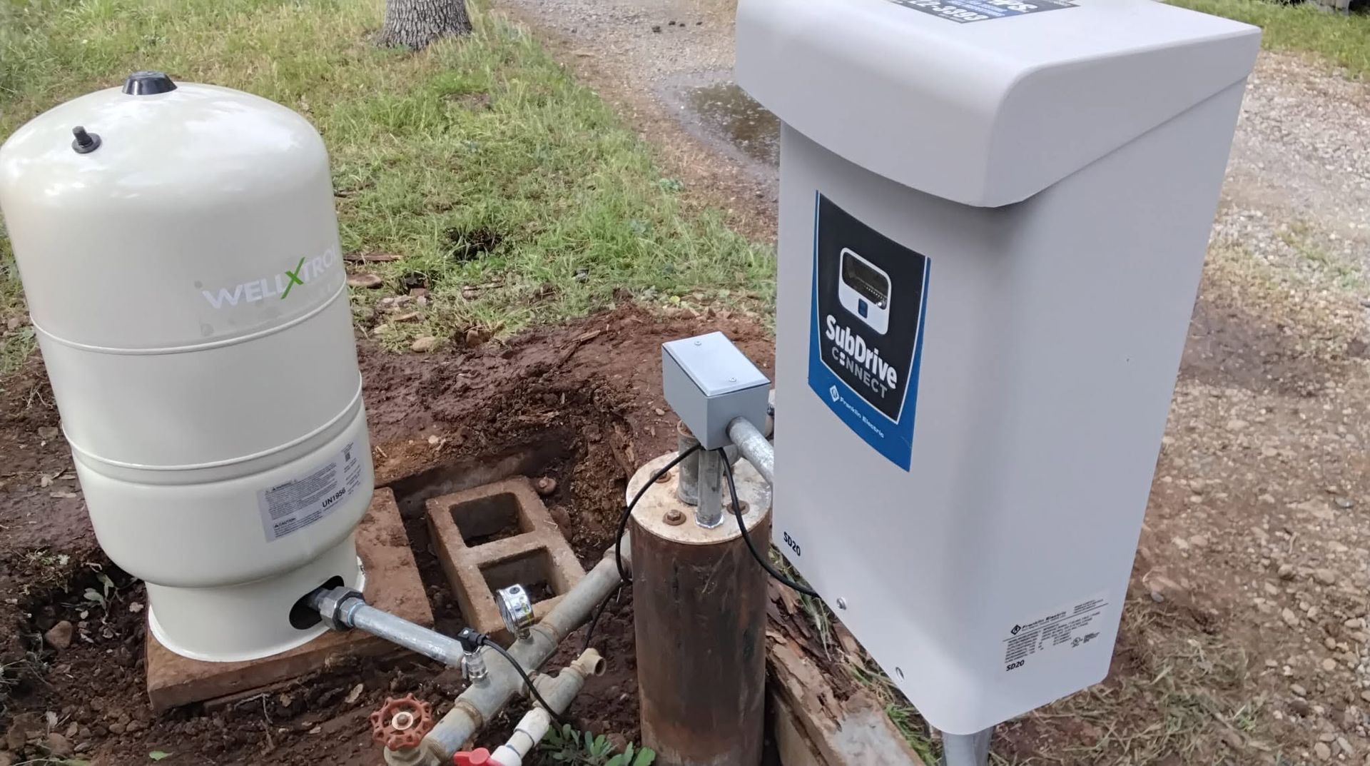Outdoor utility equipment with white tanks, pipes, and a gray service box beside a grassy area