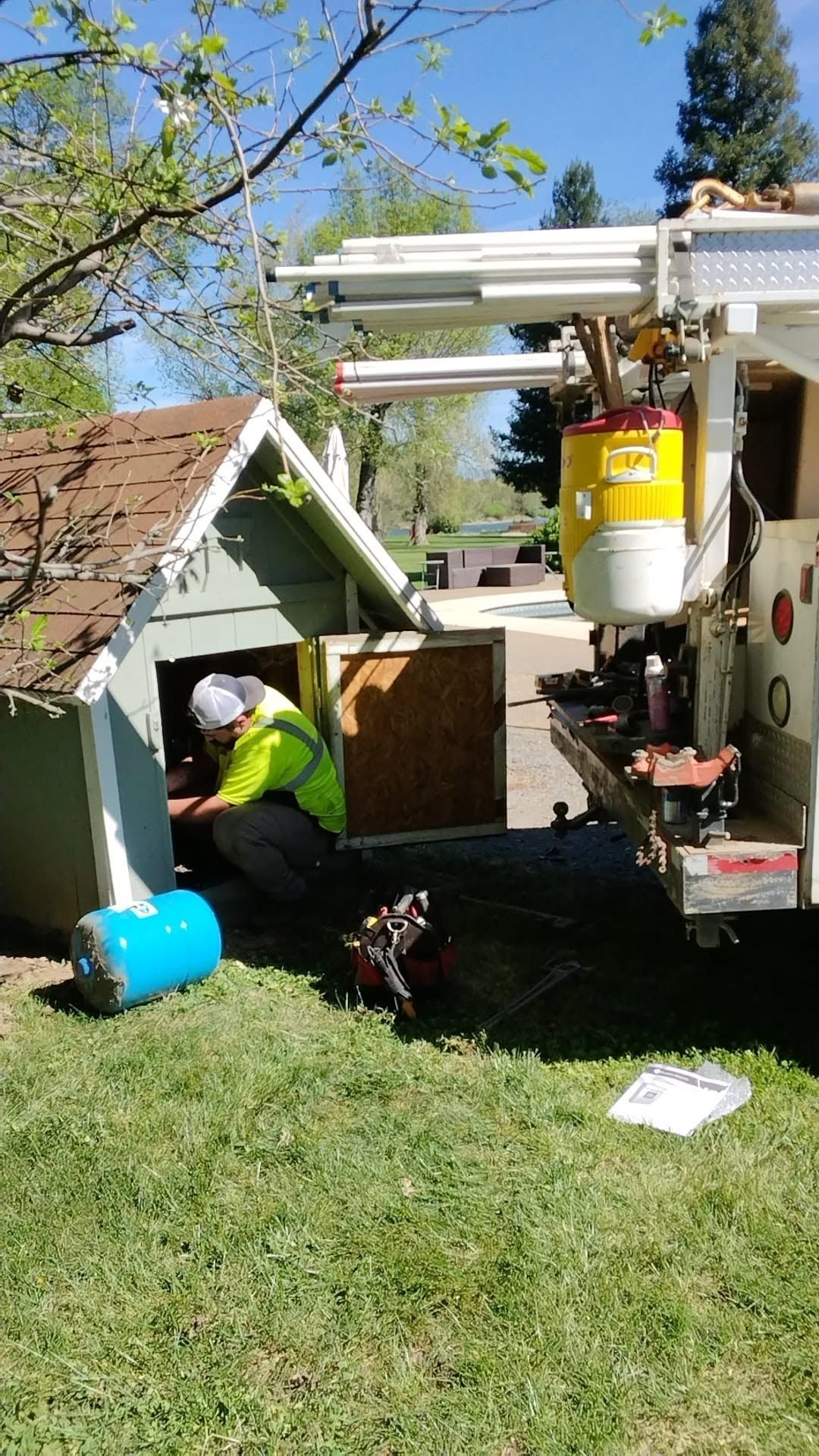 Worker in neon jacket beside utility truck lifting a large tank near a house in a grassy yard
