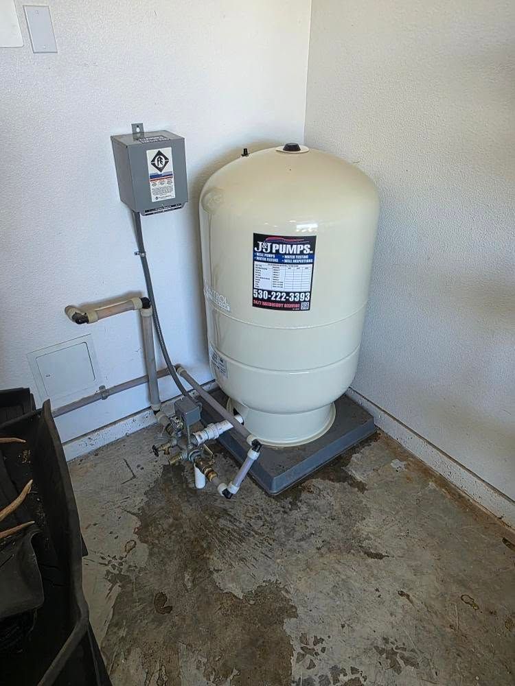 Water softener tank and control unit in a utility corner on a concrete floor.