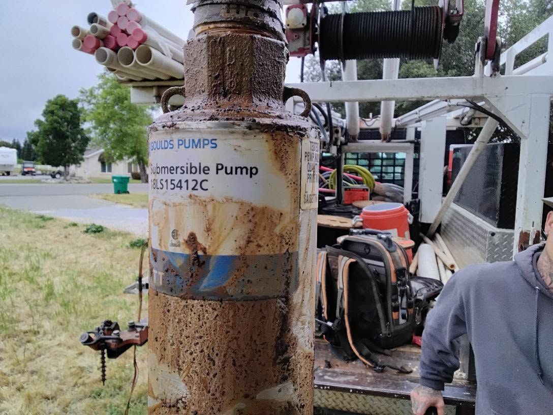 Rusty industrial pump labeled “submersible pump,” with pipes and machinery at an outdoor worksite.
