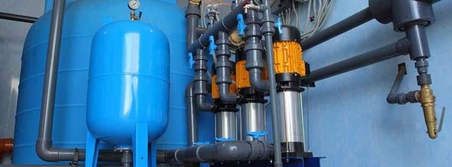 Blue industrial water filtration tanks and pipes in a mechanical room