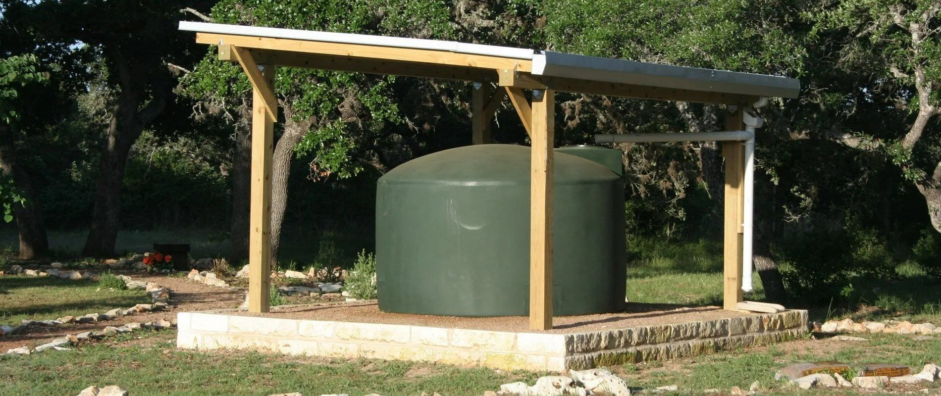 Small outdoor water tank under a simple wooden roof on a concrete base.