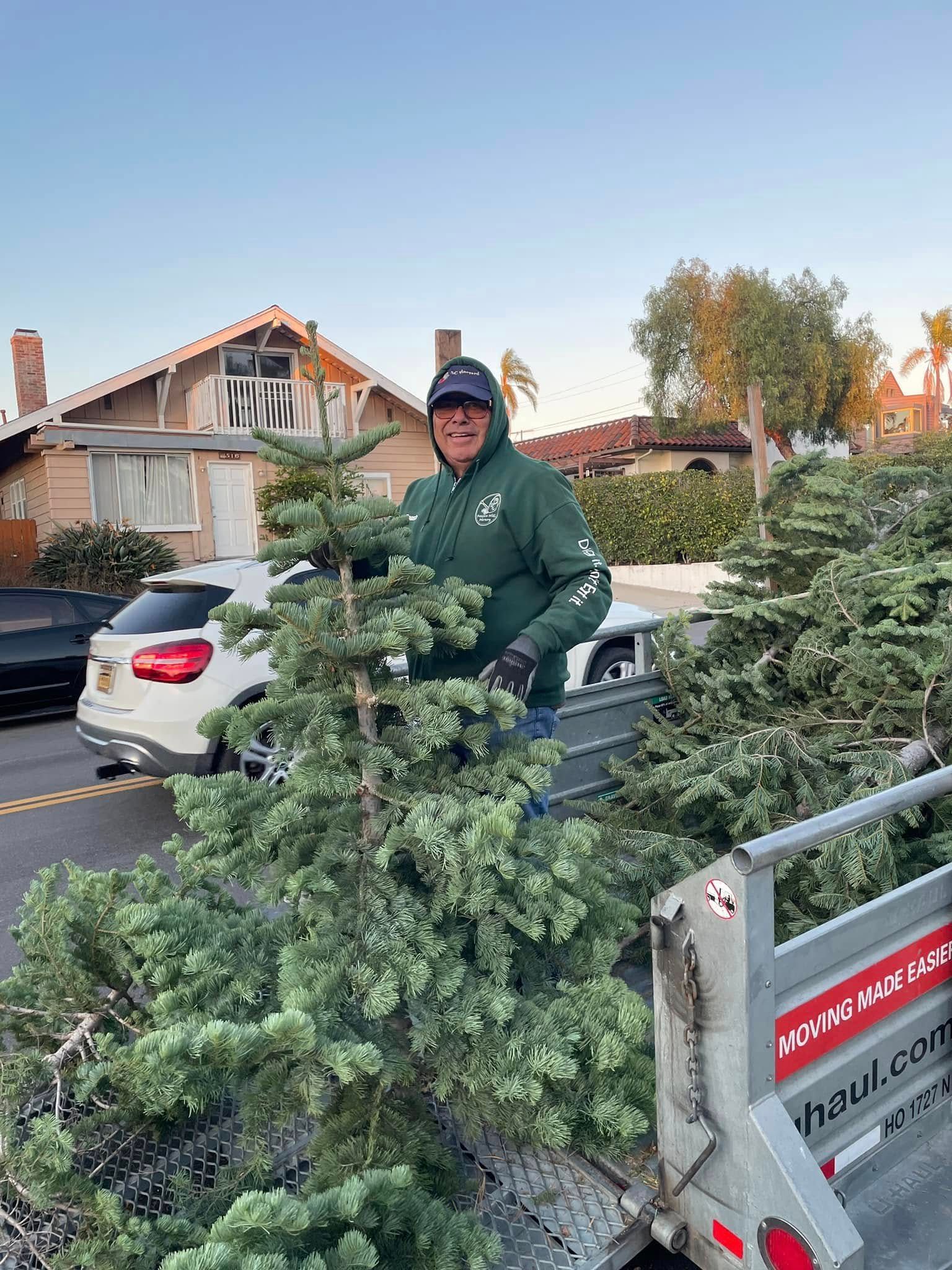 Man standing on a U-Haul truck bed with Christmas trees, houses in the background.