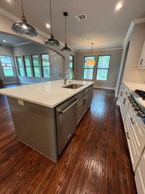 A modern kitchen features a large, gray center island with a sink and dishwasher, dark wood floors, and hanging pendants.