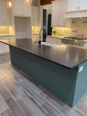 A modern kitchen featuring a teal island with a dark countertop, white cabinets, and wood-look tile flooring.