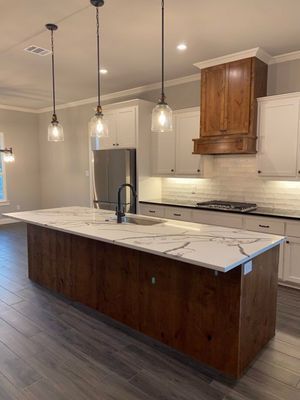 A modern kitchen with a large dark wood island, white countertops, white cabinets, and three hanging pendant lights.