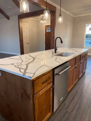 A kitchen island with a white marble-patterned countertop, wooden cabinets, and a stainless steel dishwasher.
