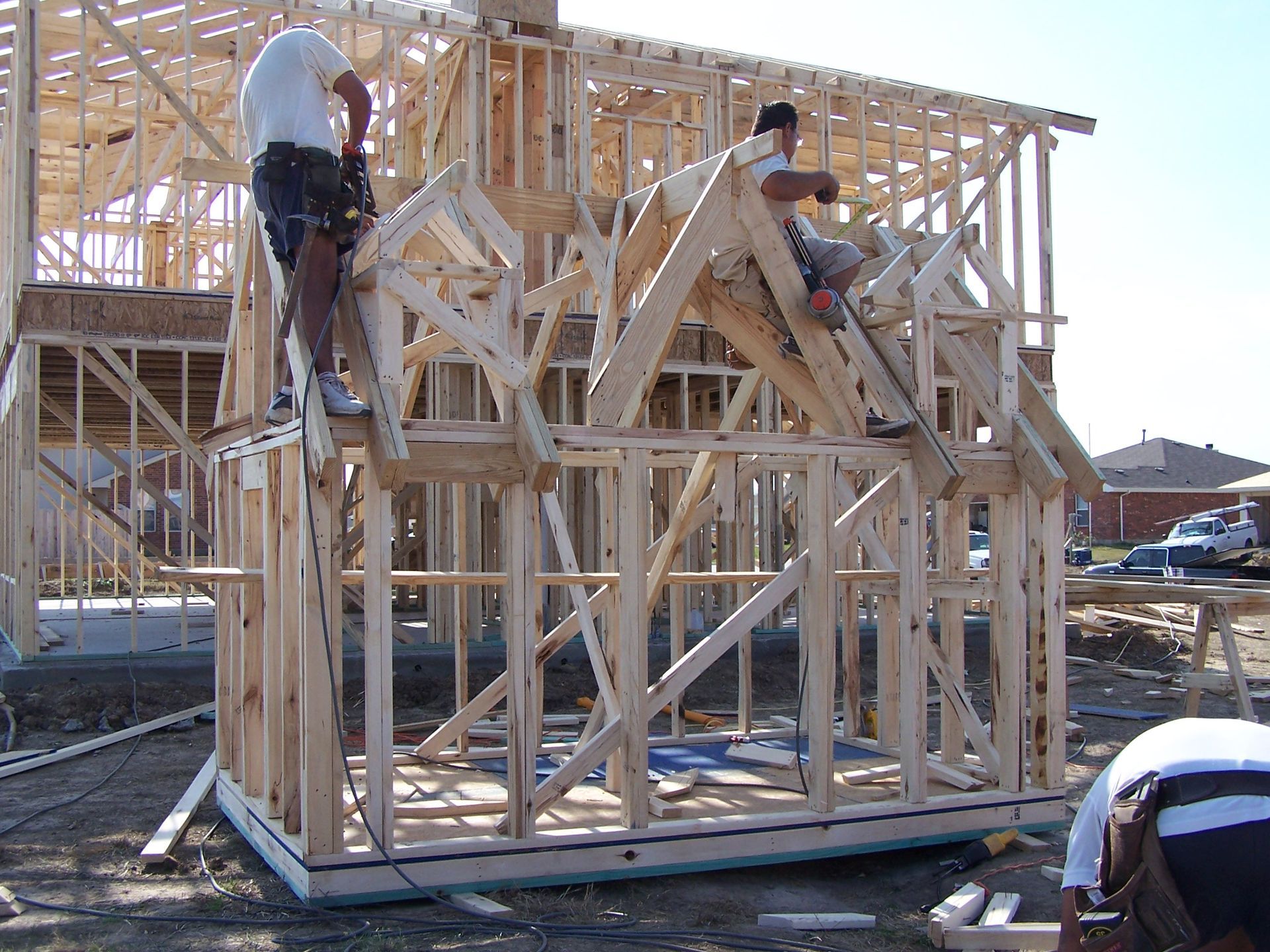 Workers frame the wood structure of a new house under construction on a bright, sunny day.