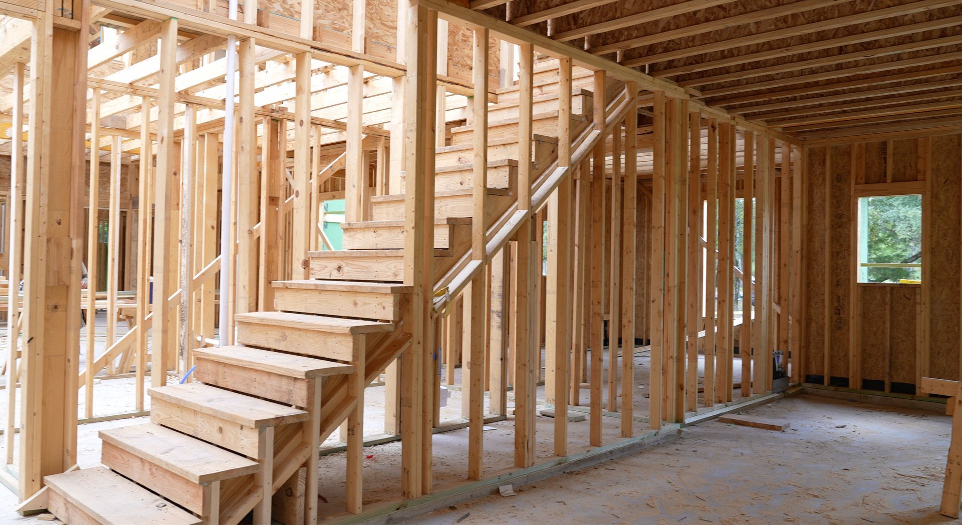 The interior of a house under construction showing wooden wall framing and a partially built staircase.
