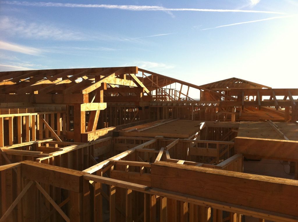 A wide view of a wood-framed building under construction at sunset, showing exposed roof trusses and interior walls.