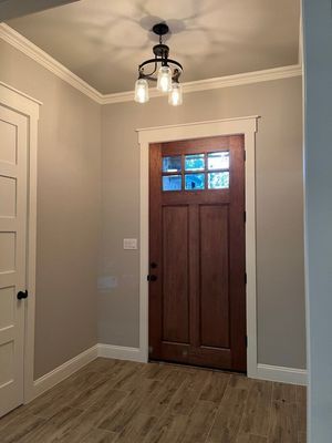 A wooden front door with glass panels in a neutral-walled foyer featuring wood-look tile floors and a ceiling light.