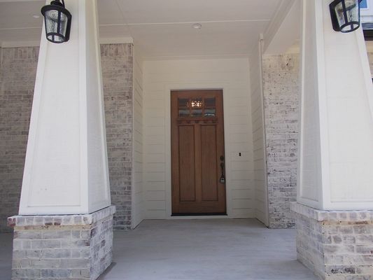 A front entryway with a wooden door flanked by two large, white-painted columns atop light brick bases under hanging lamps.