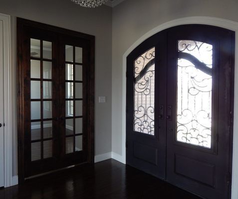 An entryway featuring a set of French doors on the left and a large, arched double entry door with iron scrollwork on right.