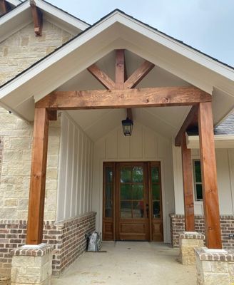 A stone and wood-trimmed front entrance of a home featuring a gable roof, timber support posts, and a wood entry door.