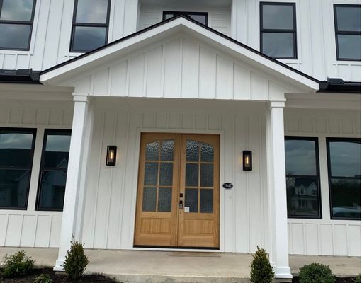 Front exterior of a white modern farmhouse featuring a double wooden door entry under a gabled porch with black accents.