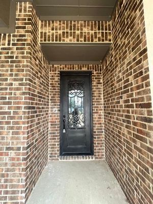 A dark brown arched wooden door with iron decorative glass is set in a recessed entryway framed by dark brown brick.