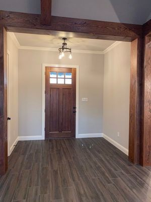 An entryway with a dark wood door and matching ceiling beams, light gray walls, and dark wood-look floor tiles.