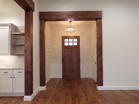 A view through a wooden-framed doorway to a front entryway with a wooden door, shiplap walls, and a hanging light.
