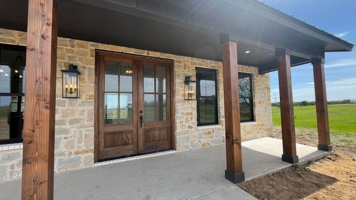 A modern farmhouse exterior with a stone facade, wooden posts, and double glass-paneled entry doors.
