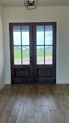 A set of dark-stained wood double doors with large glass window panes, opening to a grassy outdoor view from a tiled room.