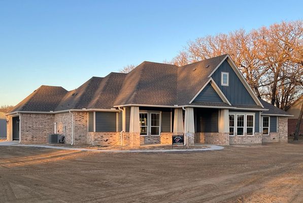 A newly built, one-story suburban home with brick and blue siding, a grey shingled roof, and unfinished dirt landscaping.