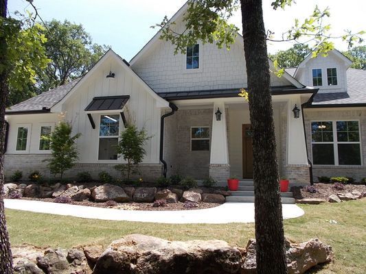 A modern home with white board-and-batten siding, stone accents, a dark roof, and a landscaped front yard with large rocks.