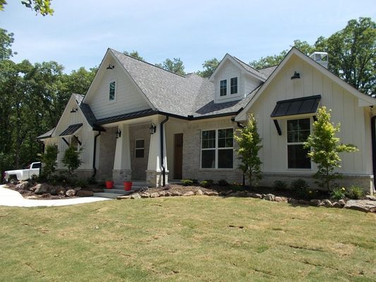 Modern single-story home with white board-and-batten siding, stone accents, black roof, and a grassy front lawn.