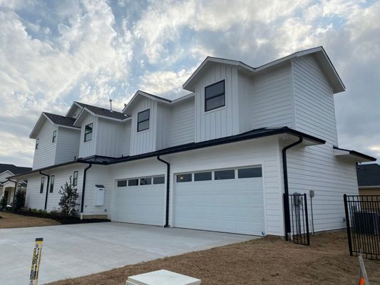 A modern white multi-family home with three garage doors under a cloudy sky.